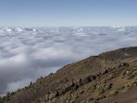 an empty road is descending above the clouds below a hill near a town on a hilltop